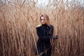 Portrait of young attractive woman in black coat and hat. Autumn landscape, dry grass