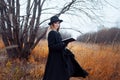 Portrait of young attractive woman in black coat and hat. She's one in a field reading book, autumn landscape, dry grass