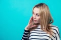 Portrait of a young attractive woman with blonde hair and makeup whispers a secret mystery in the studio on a blue