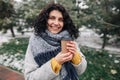 Portrait of a young attractive woman holding coffee at a snowy winter park. Female enjoys hot drink on a cold frosty winter day. Royalty Free Stock Photo