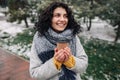 Portrait of a young attractive woman holding coffee at a snowy winter park. Female enjoys hot drink on a cold frosty winter day. Royalty Free Stock Photo