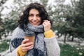 Portrait of a young attractive woman holding coffee at a snowy winter park. Female enjoys hot drink on a cold frosty winter day. Royalty Free Stock Photo