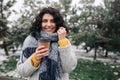 Portrait of a young attractive woman holding coffee at a snowy winter park. Female enjoys hot drink on a cold frosty winter day. Royalty Free Stock Photo