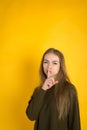 Portrait of a young attractive woman with long hair and makeup holds a finger near the lips in the studio on a yellow Royalty Free Stock Photo