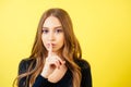 Portrait of a young attractive woman with long hair and makeup holds a finger near the lips in the studio on a yellow Royalty Free Stock Photo