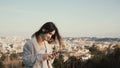 Portrait of young attractive woman standing at the panorama of Rome, Italy. Female use the smartphone outside.