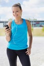 Portrait of young attractive woman standing while using and listening to music on her smartphone in park Royalty Free Stock Photo