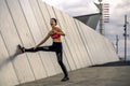 Portrait of young and attractive woman stretching next to the wall in urban park.