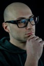 Portrait of a young bald man in black eyeglasses holding his chin with his hand while thinking looking away Royalty Free Stock Photo