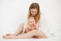 Portrait of young barefoot blond woman with little naked baby in white bedroom, after cleaning procedures. Mother caring