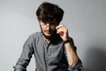 Portrait of young bearded guy with disheveled hair, touching his glasses and looking at the camera, on background of grey. Royalty Free Stock Photo