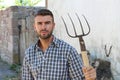 Portrait of young bearded handsome farmer in casual checkered shirt with old pitchfork on rustic background Royalty Free Stock Photo