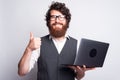 Portrait of young bearded man in suit showing thumb up and holding laptop Royalty Free Stock Photo