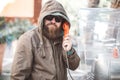 Portrait of young bearded man using public phone wearing hoodie jacket and black sunglasse