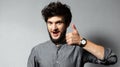 Portrait of young bearded satisfied guy with disheveled hair, shows thumbs up on background of grey. Royalty Free Stock Photo