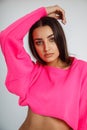 Portrait of young beauteous woman wearing short pink sweatshirt, white trousers, standing on white background. Beauty.