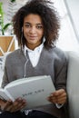 Portrait of young african american woman reading book on sofa in cafe Royalty Free Stock Photo