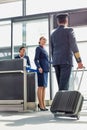 Portrait of young beautiful airport staff opening the gate for boarding while mature pilot walking in airport