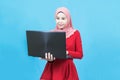 Portrait of young beautiful asian business muslim woman in red traditional dress using laptop isolated on blue background Royalty Free Stock Photo