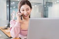 Portrait of young beautiful asian business woman in casual pink t-shirt in the office,talking on the phone and typing on laptop, Royalty Free Stock Photo