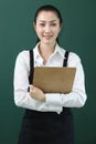 Portrait of Young beautiful Asian female barista wearing apron, holding menu and paper disposable coffee cup on green background, Royalty Free Stock Photo