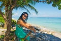 Portrait of young beautiful asian girl sitting in shade under the tree on tropical beach looking at camera Royalty Free Stock Photo