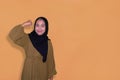 young beautiful asian muslim woman with hijab with strong hand sign on yellow background