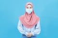 Portrait of young beautiful asian muslim woman in traditional dress wearing medical face mask isolated on blue background Royalty Free Stock Photo