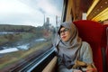 Portrait of young and beautiful Asian Muslim woman wearing glasses and hijab sitting alone against the window in a moving train Royalty Free Stock Photo