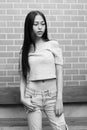 Young beautiful Asian teenage girl standing while thinking and looking down against brick wall Royalty Free Stock Photo