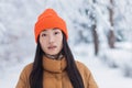 Portrait of a young beautiful Asian woman, close-up photo looking at the camera in a winter snow-covered park warmly dressed Royalty Free Stock Photo