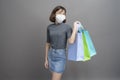 Portrait of young beautiful asian woman wearing a surgical mak is holding credit card and colorful shopping bag isolated over gray Royalty Free Stock Photo