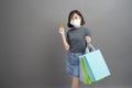 Portrait of young beautiful asian woman wearing a surgical mak is holding credit card and colorful shopping bag isolated over gray Royalty Free Stock Photo