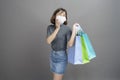 Portrait of young beautiful asian woman wearing a surgical mak is holding credit card and colorful shopping bag isolated over gray Royalty Free Stock Photo