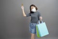 Portrait of young beautiful asian woman wearing a surgical mak is holding credit card and colorful shopping bag isolated over gray Royalty Free Stock Photo