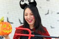 Portrait of young beautiful asian woman wearing witch costume holding pumpkin Jack O Lantern and trident on white brick background Royalty Free Stock Photo