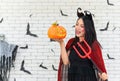 Portrait of young beautiful asian woman wearing witch costume holding pumpkin Jack O Lantern and trident on white brick background Royalty Free Stock Photo