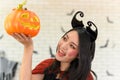 Portrait of young beautiful asian woman wearing witch costume holding pumpkin Jack O Lantern on white brick background decorated Royalty Free Stock Photo