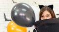 Portrait of young beautiful asian woman wearing witch costume posing with balloons on white brick background decorated with black Royalty Free Stock Photo
