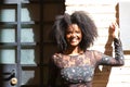 Portrait of young, beautiful black woman with afro hair and black dress with flowers is leaning against the wall of a building in Royalty Free Stock Photo