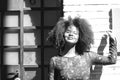 Portrait of young, beautiful black woman with afro hair and black dress with flowers is leaning against the wall of a building in Royalty Free Stock Photo