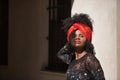 Portrait of a young, beautiful and black woman with afro hair, with a floral dress and scarf in her hair, leaning on a wall Royalty Free Stock Photo