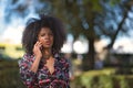 Portrait of a young, beautiful black woman with afro hair, wearing a floral shirt, talking on her mobile phone in the street. Royalty Free Stock Photo