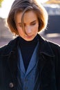 Young blond short-haired woman in velvet coat, vest and sweater on sunny street Royalty Free Stock Photo