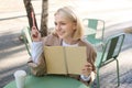 Portrait of young beautiful blond woman, artsy girl in coffee shop, holding notebook and pen, writing in her journal