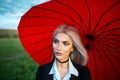 Portrait of young beautiful blonde girl, holding red umbrella, wearing black suit with choker on neck. Royalty Free Stock Photo