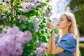 Portrait of a young beautiful blonde posing among blooming lilacs. The girl enjoys the fragrance of flowers, holds in her hands in Royalty Free Stock Photo