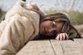 Portrait of young, beautiful, blonde woman with coat, sitting on a wooden bench with her head resting on the table, with serious Royalty Free Stock Photo