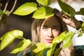 Portrait of young, beautiful, blonde woman with green eyes, looking through the green leaves of a plant. Concept beauty, eyes, Royalty Free Stock Photo