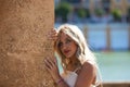 Portrait of a young, beautiful blonde woman leaning her hands on a brown wall with a shy look and bright eyes. The woman is Royalty Free Stock Photo